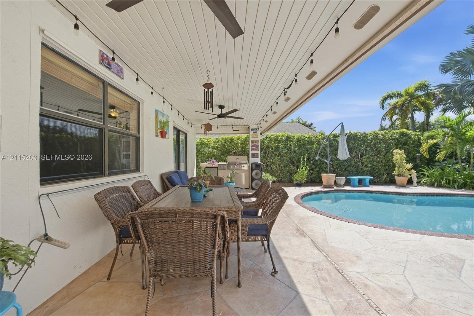 Covered patio featuring a tongue-and-groove ceiling, stone-tiled flooring, built-in outdoor kitchen, string lighting, and an inground pool with a stone deck Covered patio featuring a tongue-and-groove ceiling, stone-tiled flooring, built-in outdoor kitchen, string lighting, and an inground pool with a stone deck