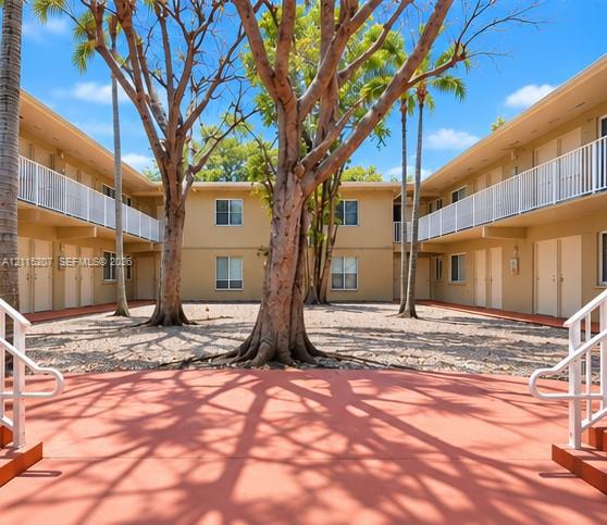 Central courtyard featuring gravel ground cover, mature trees, two-story exterior walls, and white metal balcony railings