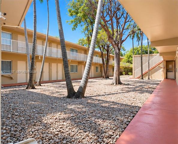Open-air courtyard featuring gravel ground cover, mature palm trees, tiered exterior walkways with white metal railings, and a concrete staircase Open-air courtyard featuring gravel ground cover, mature palm trees, tiered exterior walkways with white metal railings, and a concrete staircase