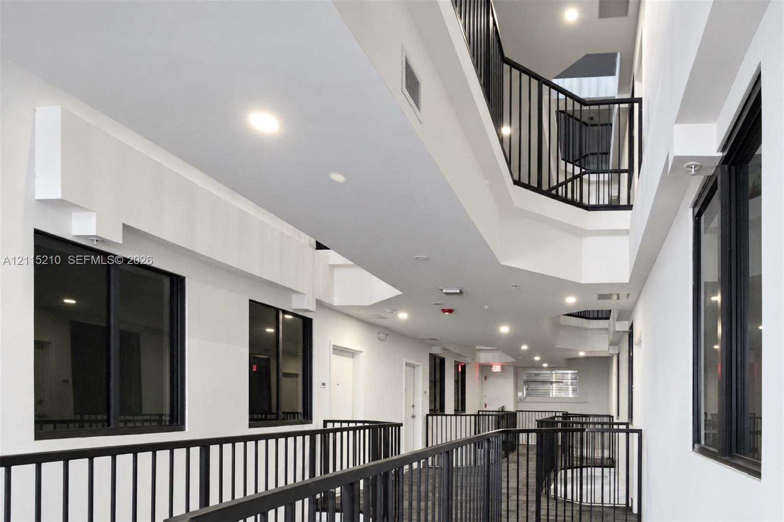 Multi-level walkway featuring black metal railings, recessed ceiling lighting, and large windows with black frames