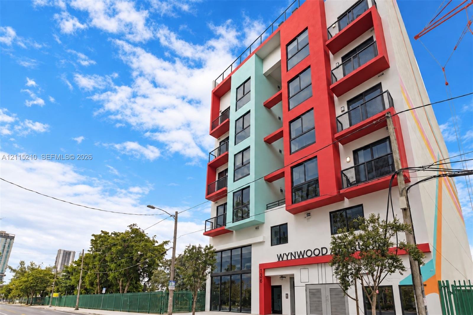 Multi-story contemporary exterior featuring a bold red and teal facade, private balconies with glass railings, floor-to-ceiling ground-level windows, and a flat roofline