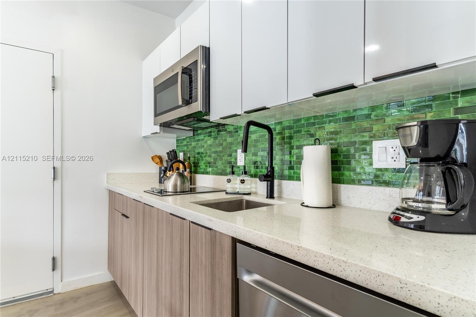 Kitchen featuring white high-gloss upper cabinetry, wood-finish lower cabinetry, stone-composite countertops, a glass subway-tile backsplash, and a matte black gooseneck faucet