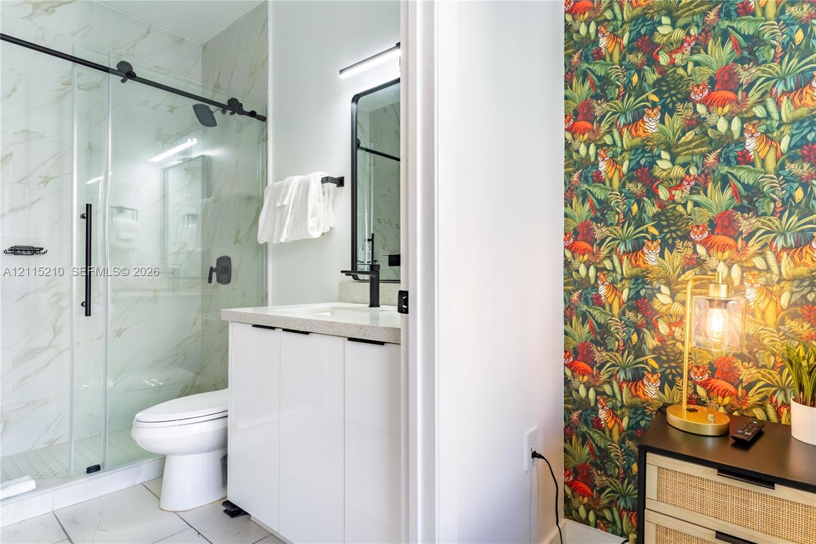 Bathroom featuring a glass-enclosed shower with sliding hardware, stone-finish countertop, white cabinetry, matte black fixtures, and large-format tile flooring