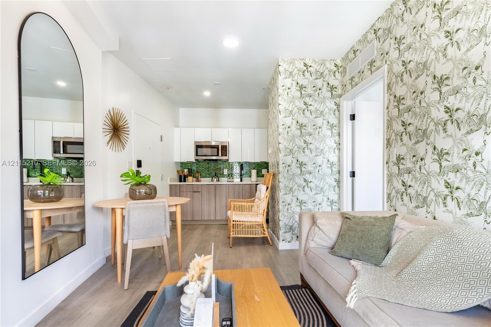 Kitchen featuring white upper cabinetry, wood-finish lower cabinetry, green tile backsplash, and a built-in microwave, complemented by wood-finish flooring and patterned wall coverings