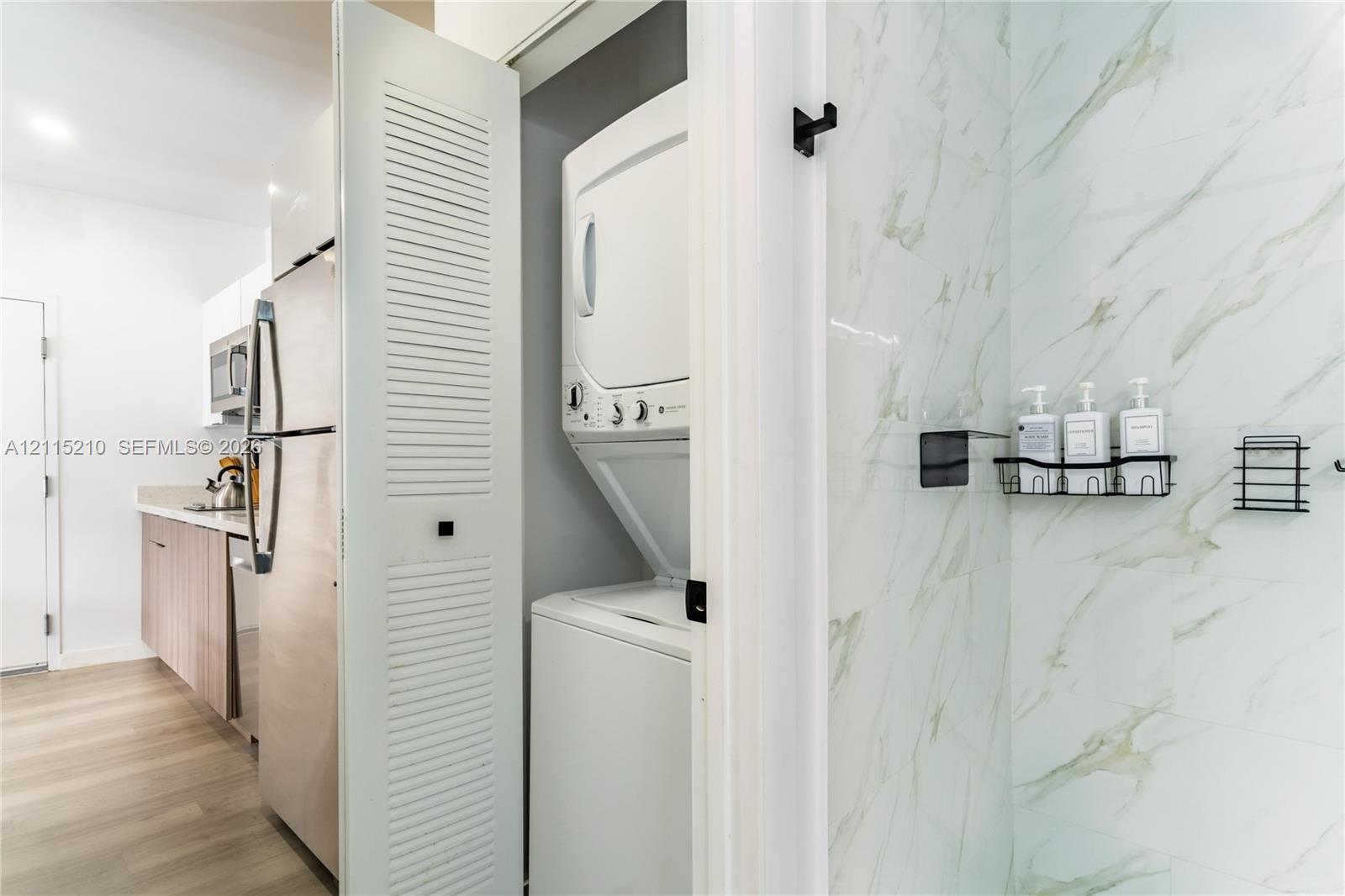 Stacked laundry unit concealed behind louvered doors, stone-finish wall tile, and built-in matte black wall-mounted shelving