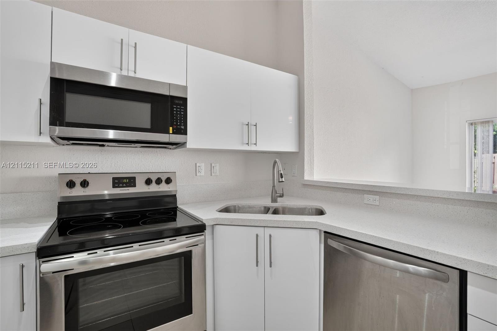 Kitchen featuring white flat-panel cabinetry, stainless steel appliances, a range with a glass cooktop, solid-surface countertops, and a dual-basin stainless steel sink