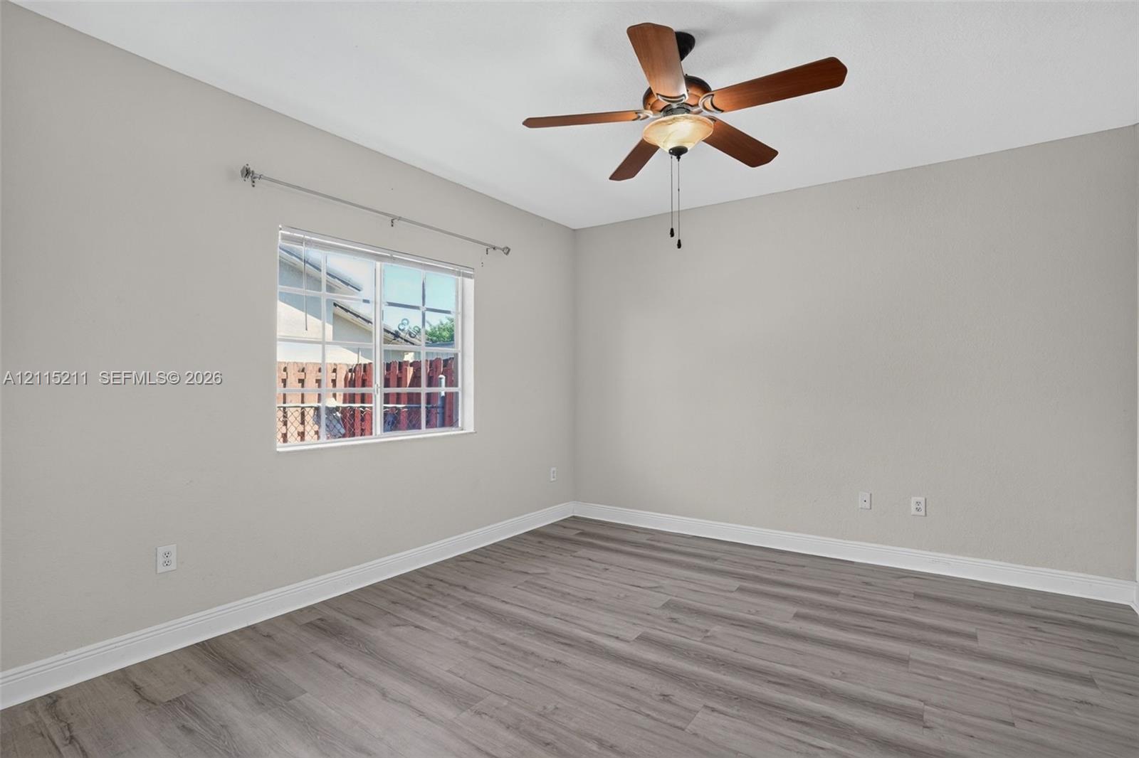 Room featuring wood-finish flooring, neutral wall paint, multi-pane window, and ceiling fan with integrated light fixture