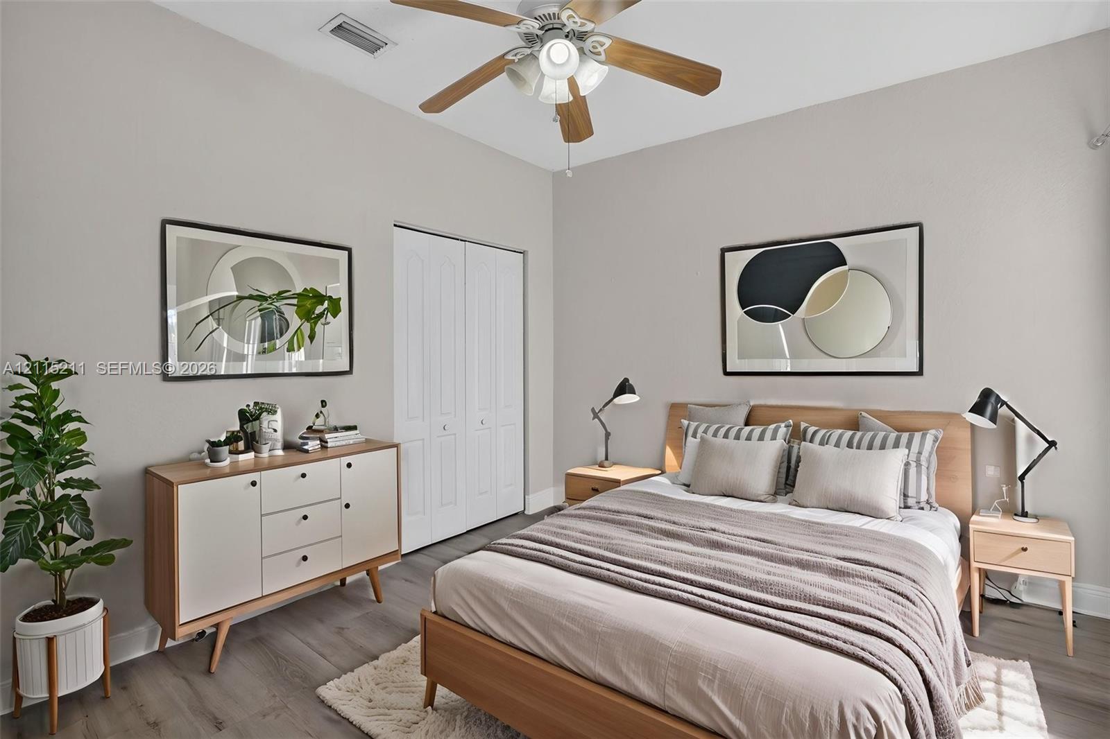 Neutral-toned interior featuring wood-finish flooring, a ceiling fan with integrated lighting, and a double-door closet with paneled detailing
