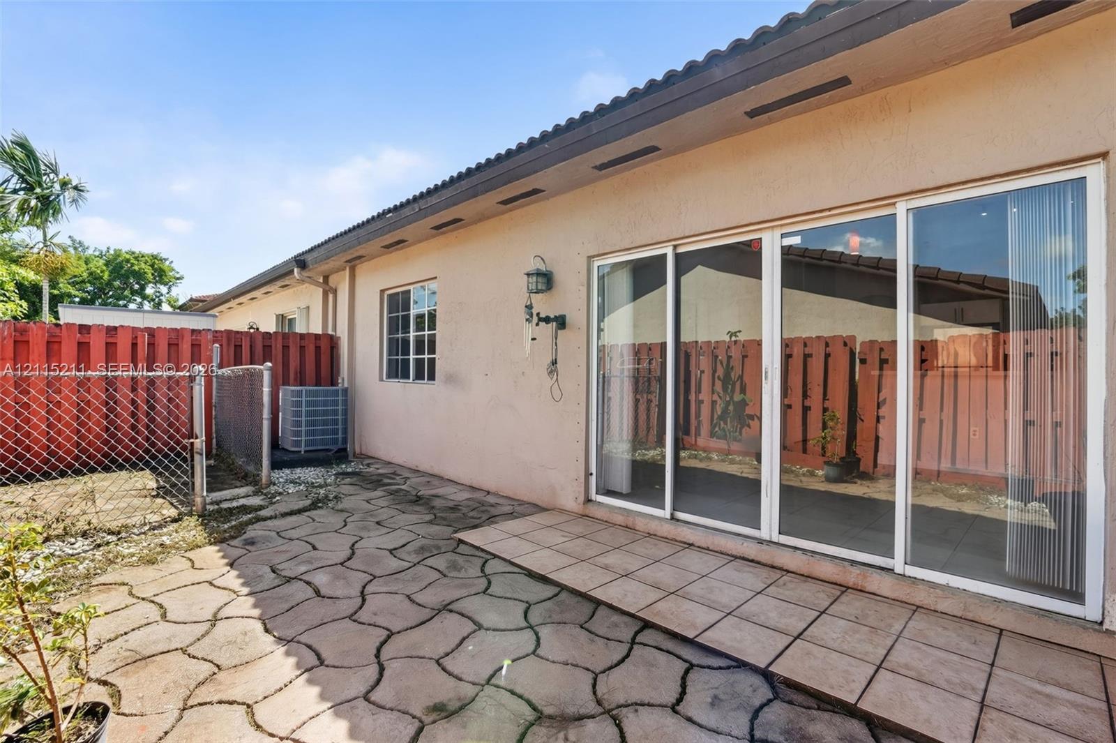 Rear exterior featuring a concrete paver patio, tiled landing, sliding glass doors, and perimeter wood fencing