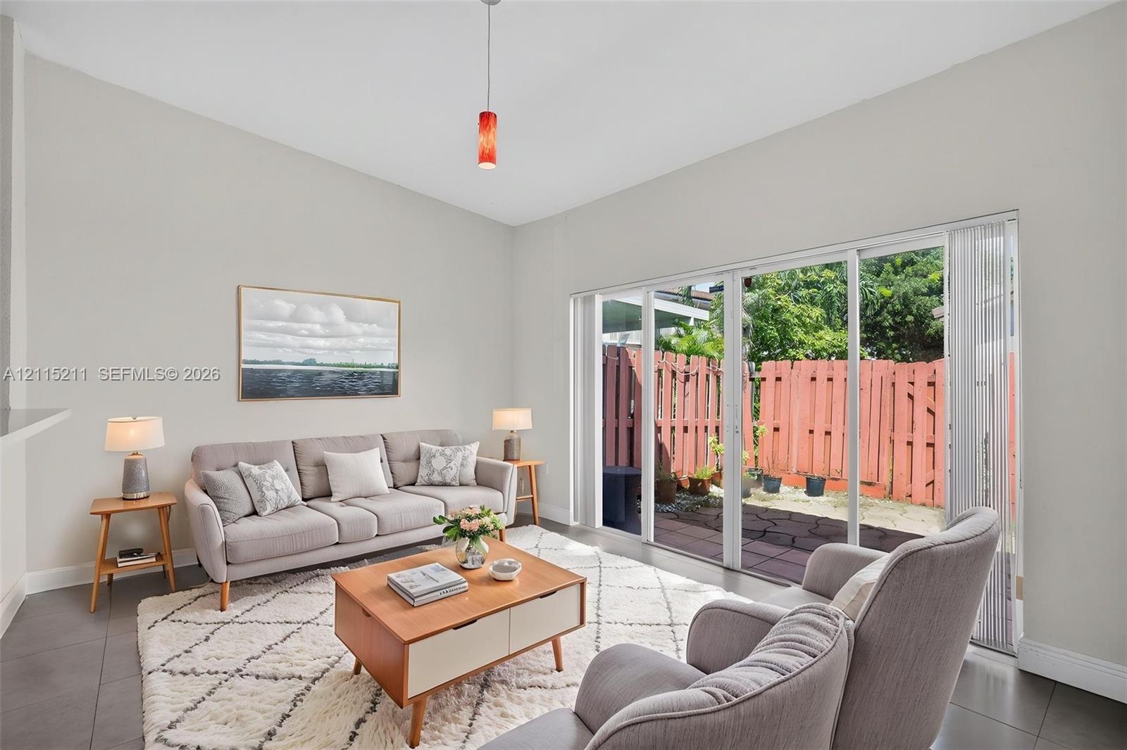 Living space featuring vaulted ceilings, large-format tile flooring, a glass pendant light, and a set of sliding glass doors opening to a fenced-in patio