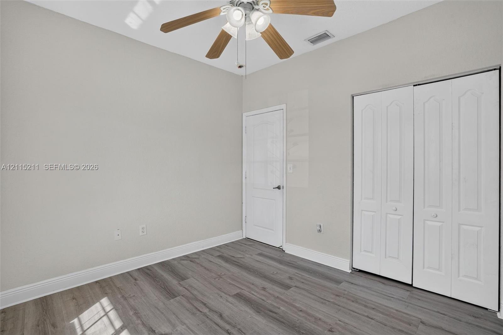 Neutral-toned room featuring wood-finish flooring, a vaulted ceiling, a ceiling fan with integrated lighting, and a bi-fold closet