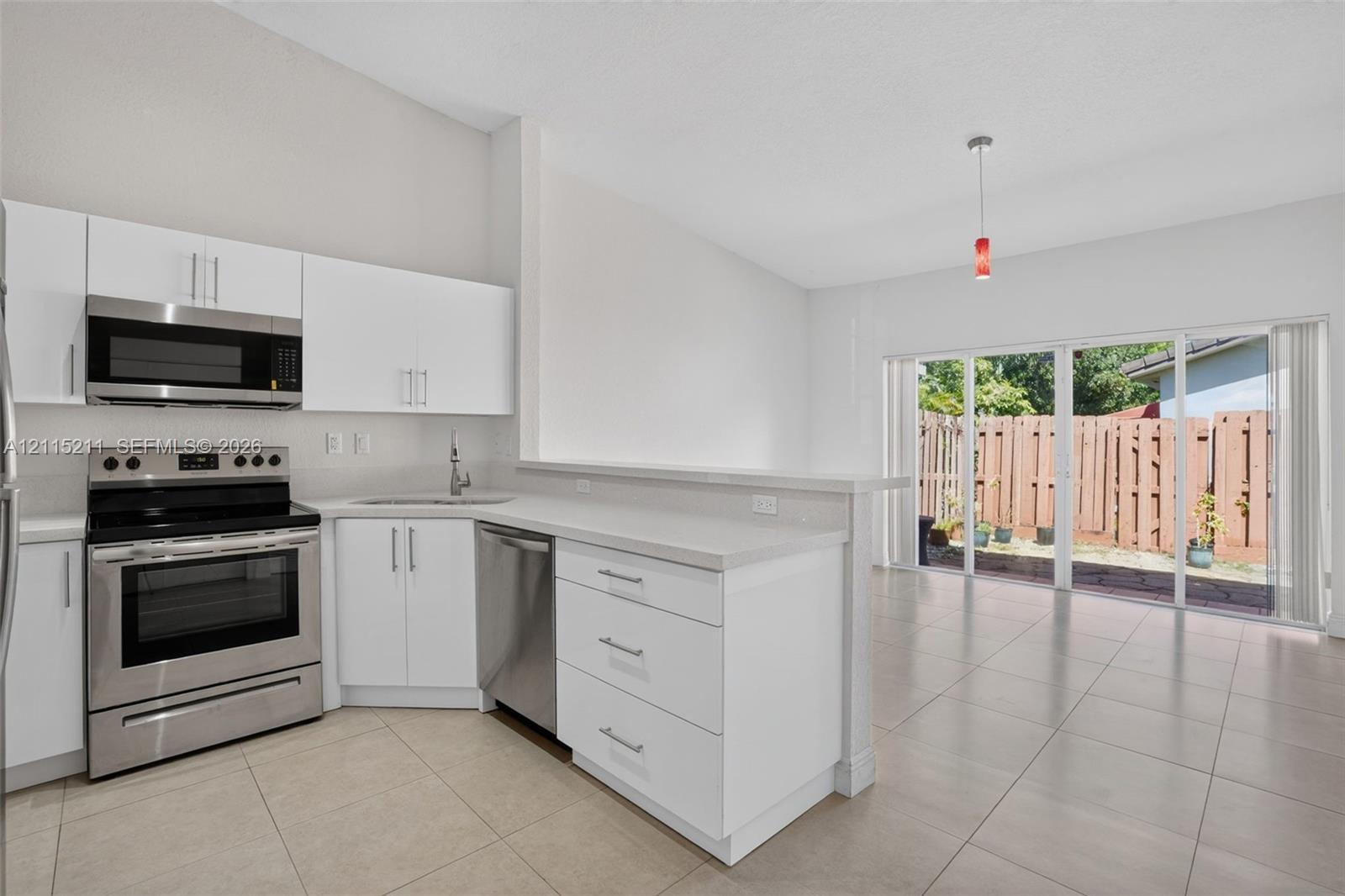 Kitchen featuring white cabinetry, neutral countertops, stainless steel appliances, tile flooring, and sliding glass doors