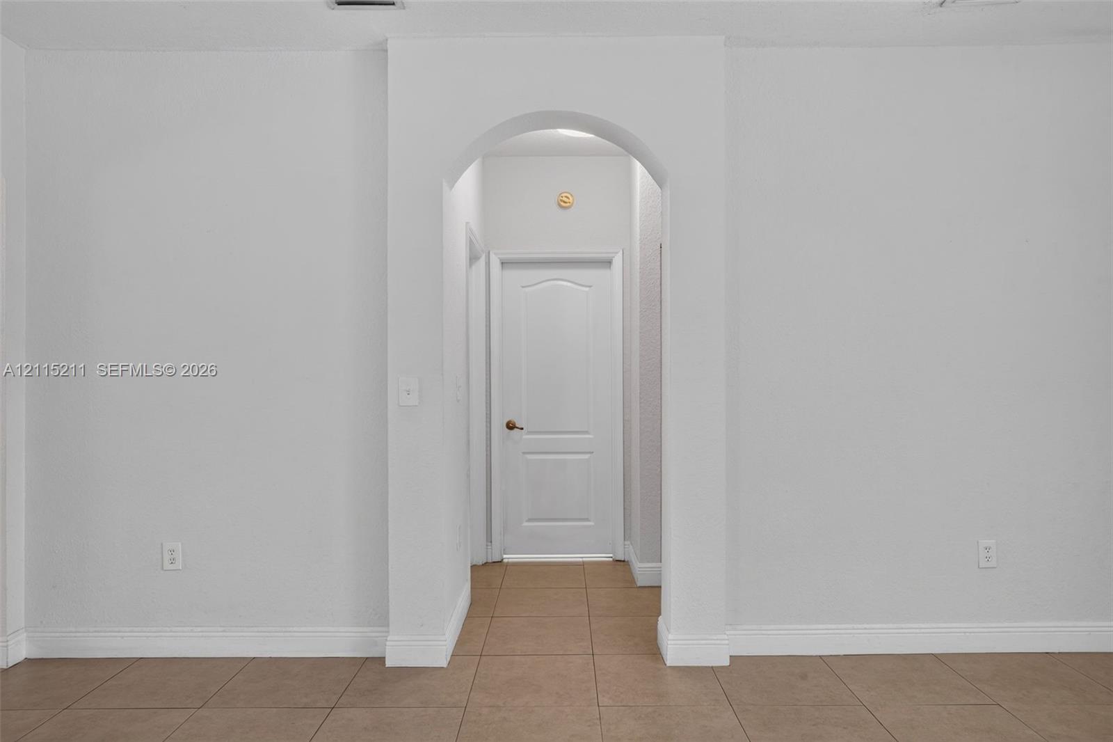 Arched doorway featuring a six-panel interior door and neutral tile flooring