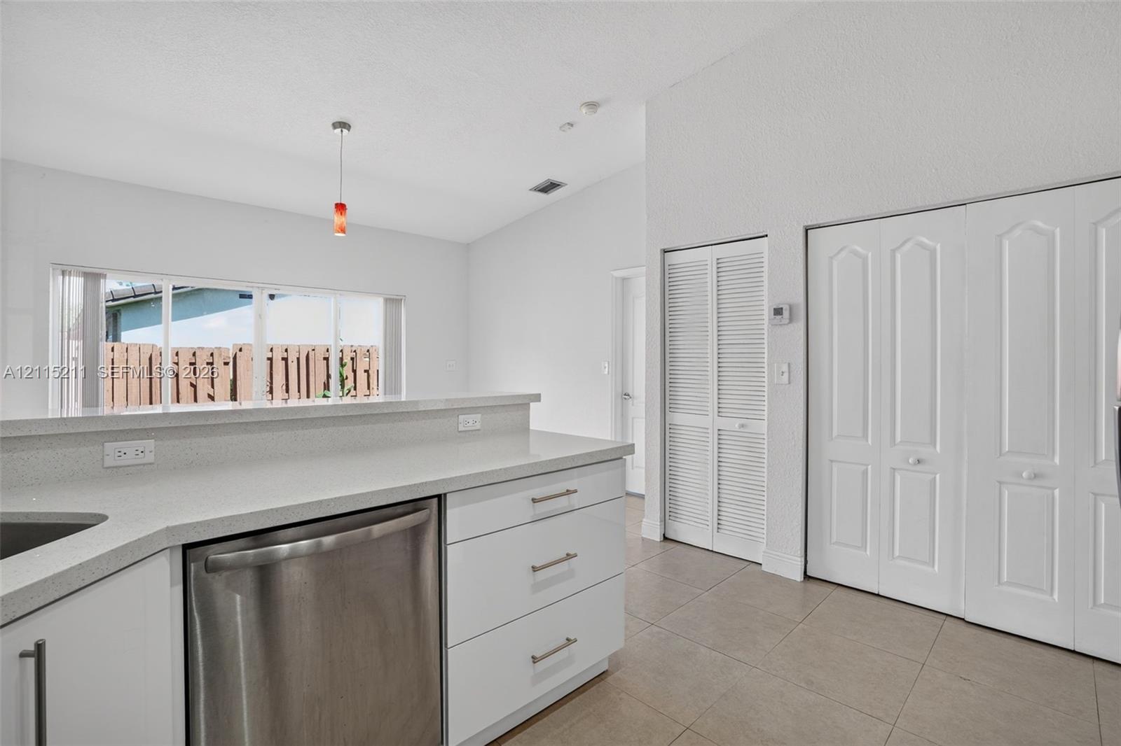 Kitchen featuring a peninsula with solid-surface countertops, stainless steel dishwasher, tile flooring, vaulted ceilings, and louvered-style closet doors
