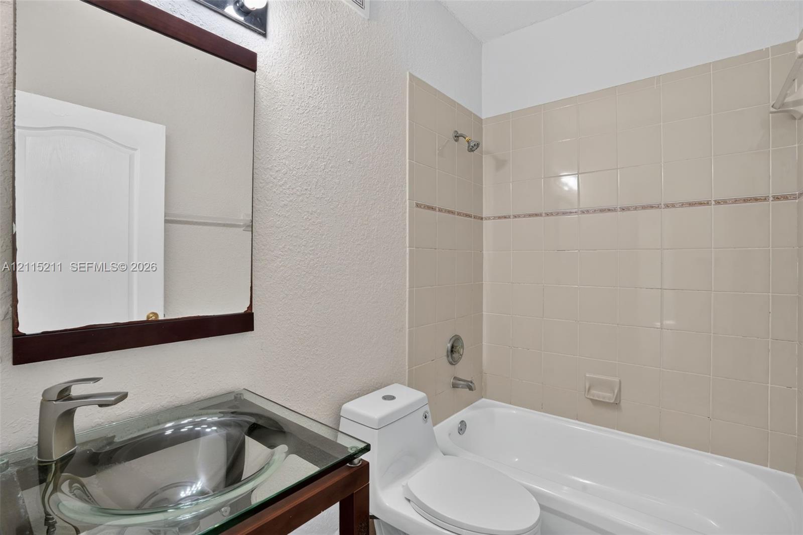 Glass vessel sink with a brushed-nickel faucet, dark-finish vanity, framed wall mirror, and tub-shower combination with ceramic tile surround