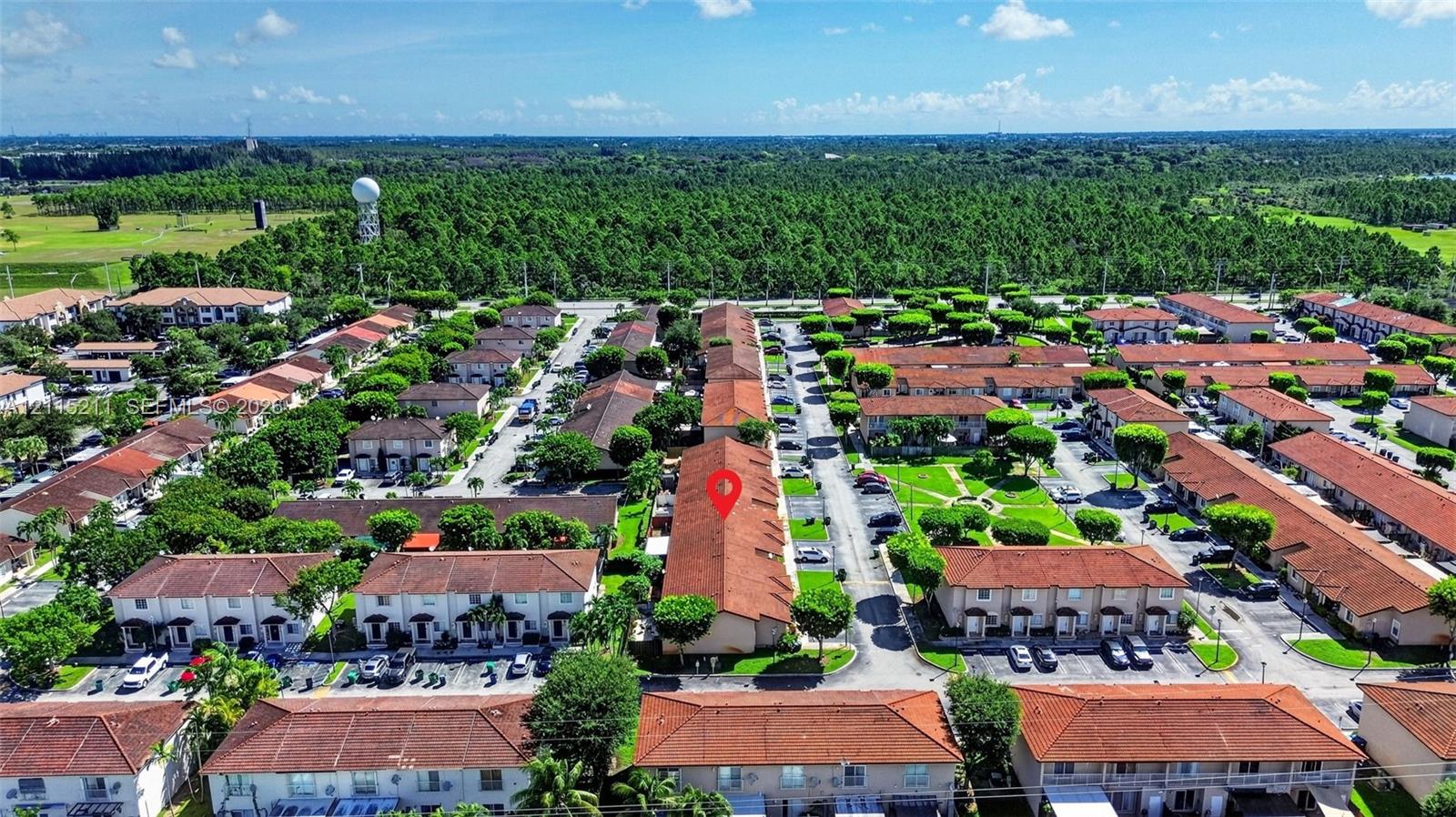 Aerial perspective of a multi-unit residential community featuring terracotta-style roofing, paved parking areas, and abundant mature landscaping