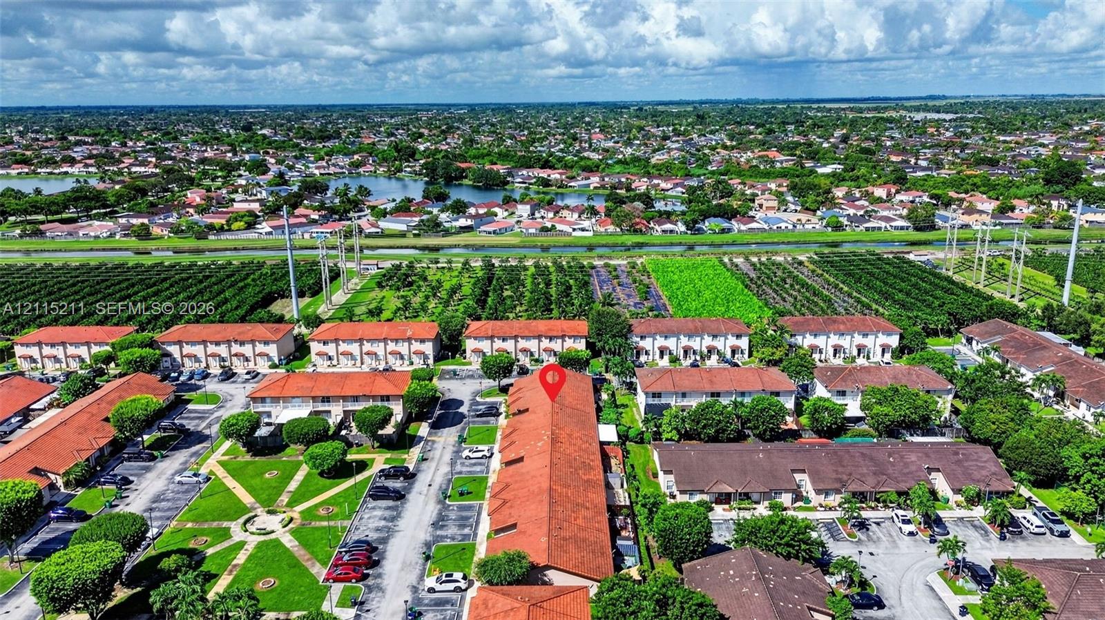 Aerial perspective of a multi-unit residential complex featuring terracotta tile roofing, manicured green space, paved parking areas, and mature landscaping