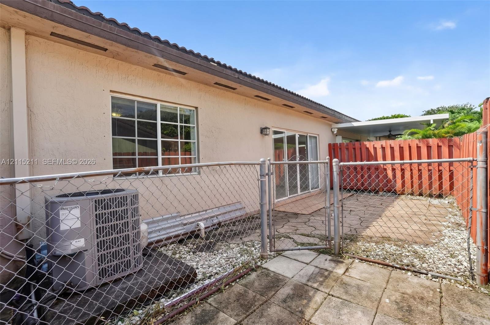 Stucco exterior featuring sliding glass doors, a chain-link fenced perimeter, concrete paver patio, and privacy fencing