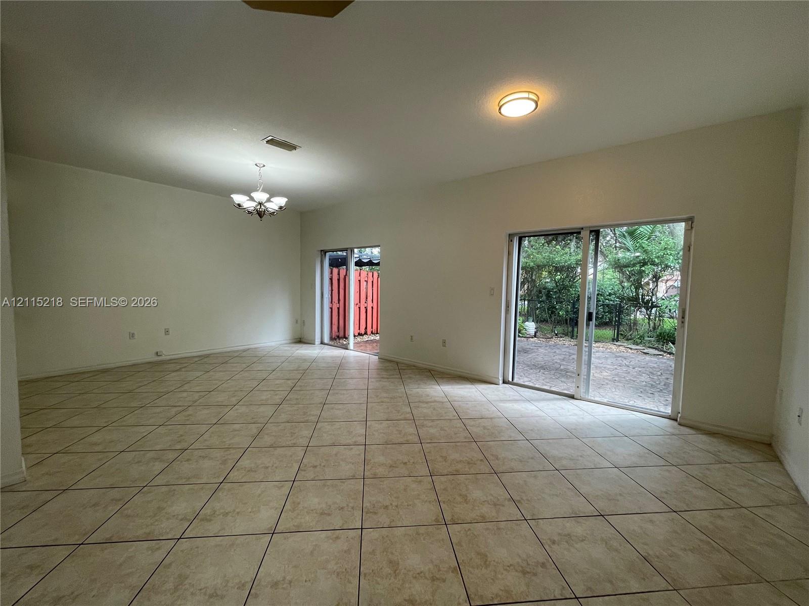 Spacious interior featuring ceramic tile flooring, a recessed tray ceiling, a multi-light chandelier, and sliding glass doors leading to the exterior Spacious interior featuring ceramic tile flooring, a recessed tray ceiling, a multi-light chandelier, and sliding glass doors leading to the exterior
