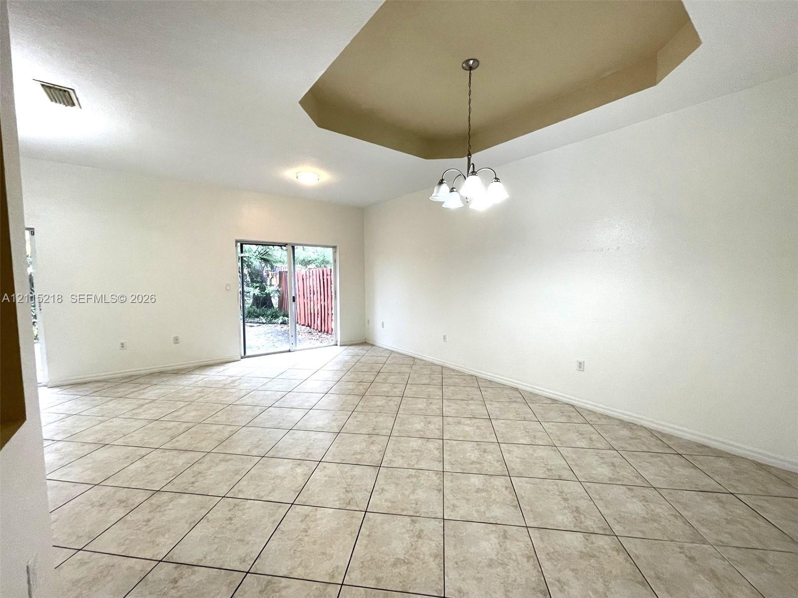 Spacious interior featuring ceramic tile flooring, a recessed tray ceiling, a multi-light chandelier, and sliding glass doors leading to the exterior Spacious interior featuring ceramic tile flooring, a recessed tray ceiling, a multi-light chandelier, and sliding glass doors leading to the exterior