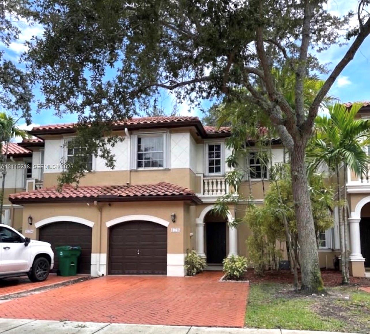 Two-story Mediterranean-style exterior featuring a terracotta tile roof, arched garage entries, stucco finish, stone-detailed balcony railing, and paved driveway Two-story Mediterranean-style exterior featuring a terracotta tile roof, arched garage entries, stucco finish, stone-detailed balcony railing, and paved driveway