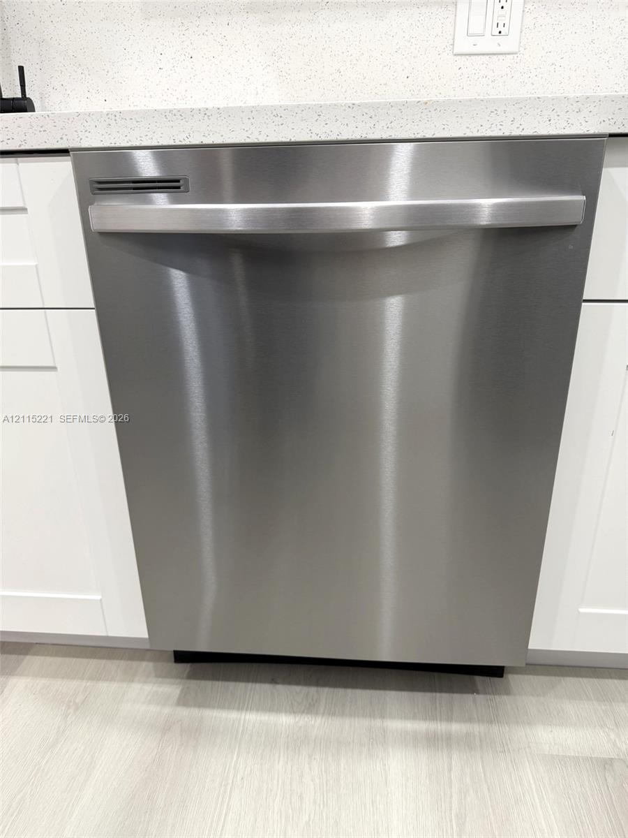 Stainless steel dishwasher featuring a horizontal handle and integrated controls, accented by shaker-style cabinetry and a neutral-toned stone-finish countertop