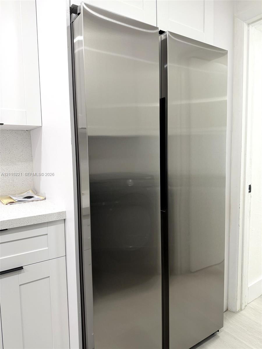 Stainless steel side-by-side refrigerator, white shaker-style cabinetry, solid-surface countertop, and flat-panel hardware