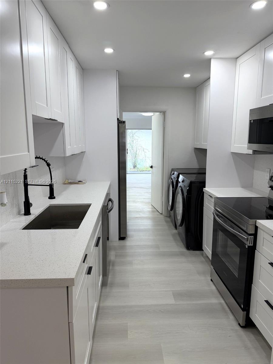 White shaker-style cabinetry, quartz countertops, stainless steel appliances, matte black hardware, and light-tone wood-finish flooring