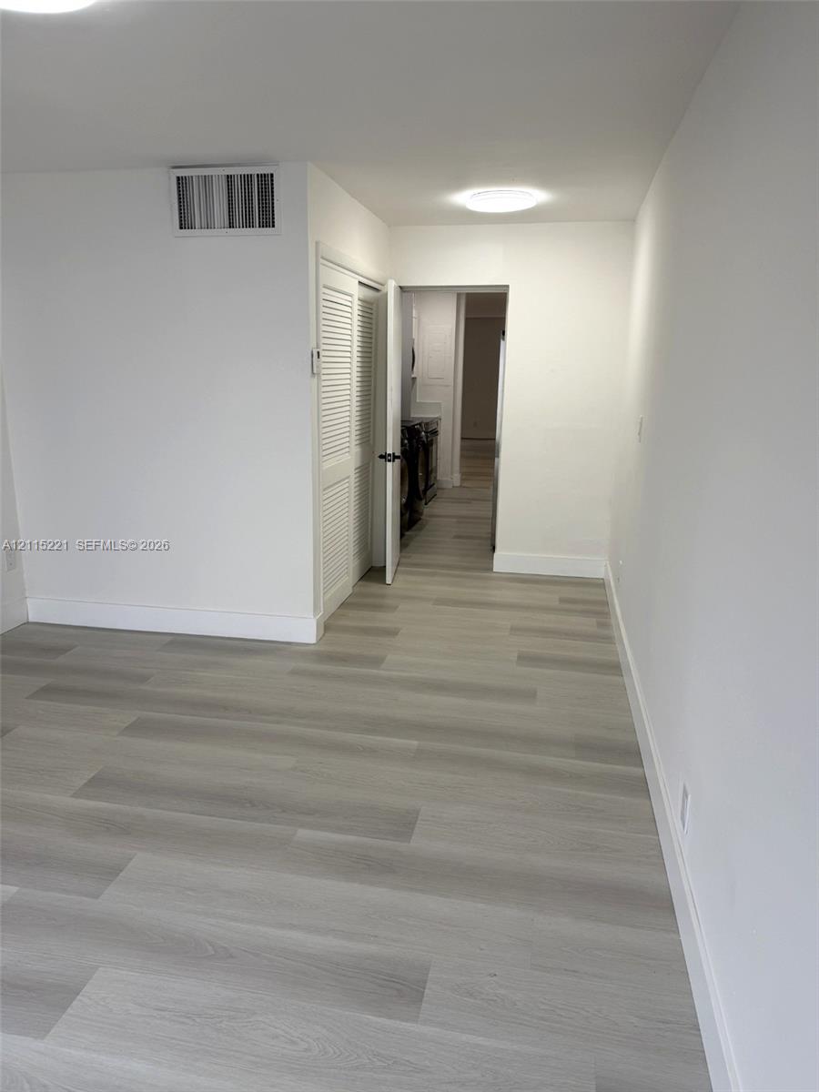 Neutral interior space featuring wood-finish flooring, crisp white walls, flush-mount ceiling lighting, and louvered closet doors
