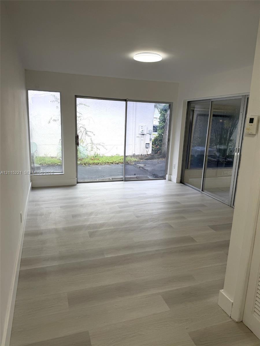 Interior space featuring light-toned wood-finish flooring, dual sliding glass doors, a floor-to-ceiling side window, and a flush-mount overhead light fixture