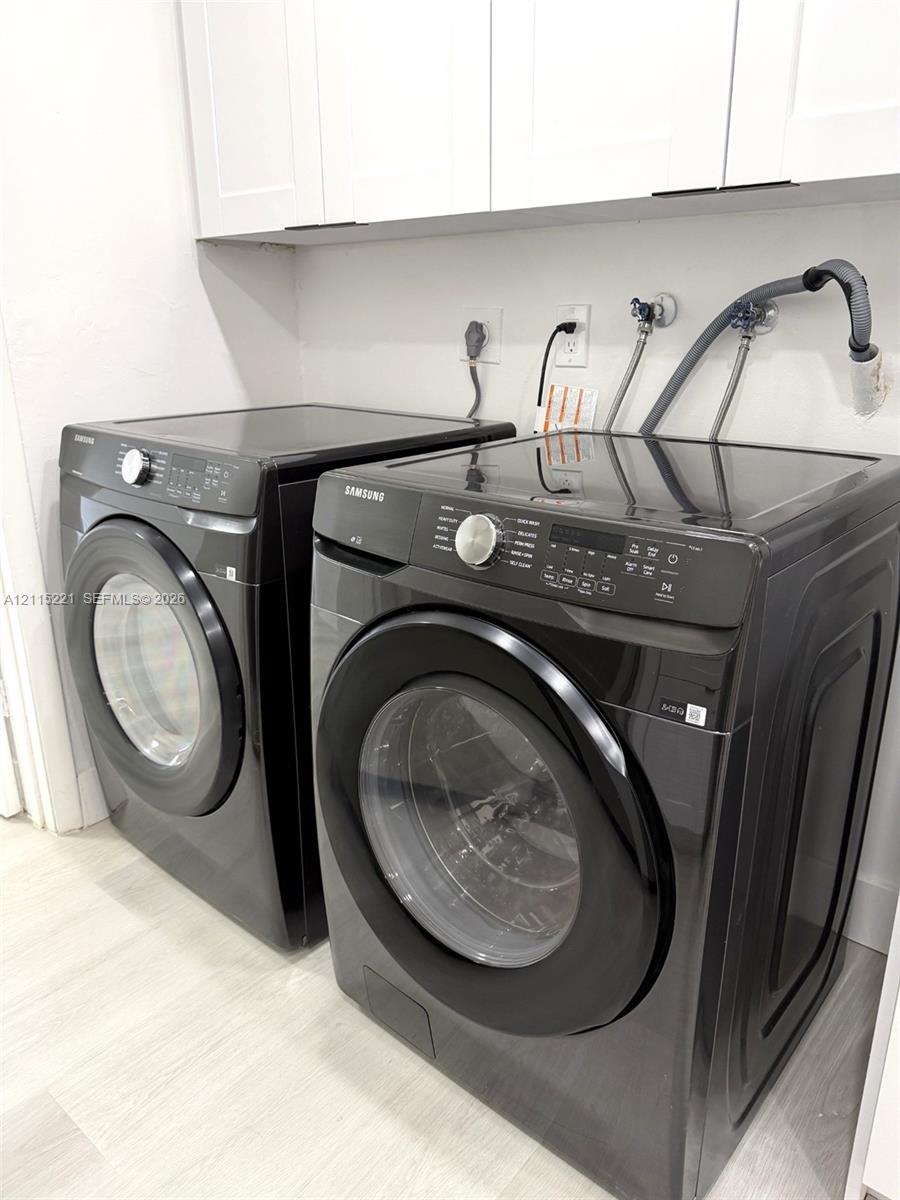 Laundry area featuring crisp white upper cabinetry, wood-finish flooring, and black-finish front-loading appliances