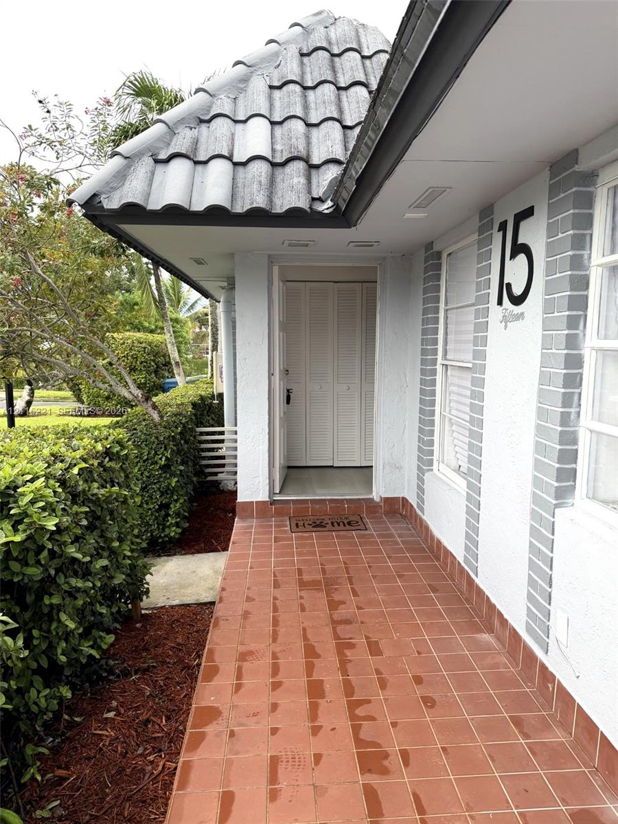 Covered entryway featuring terra cotta tile flooring, a hipped roofline with concrete tiles, white louvered entry doors, and contrasting painted brick accents
