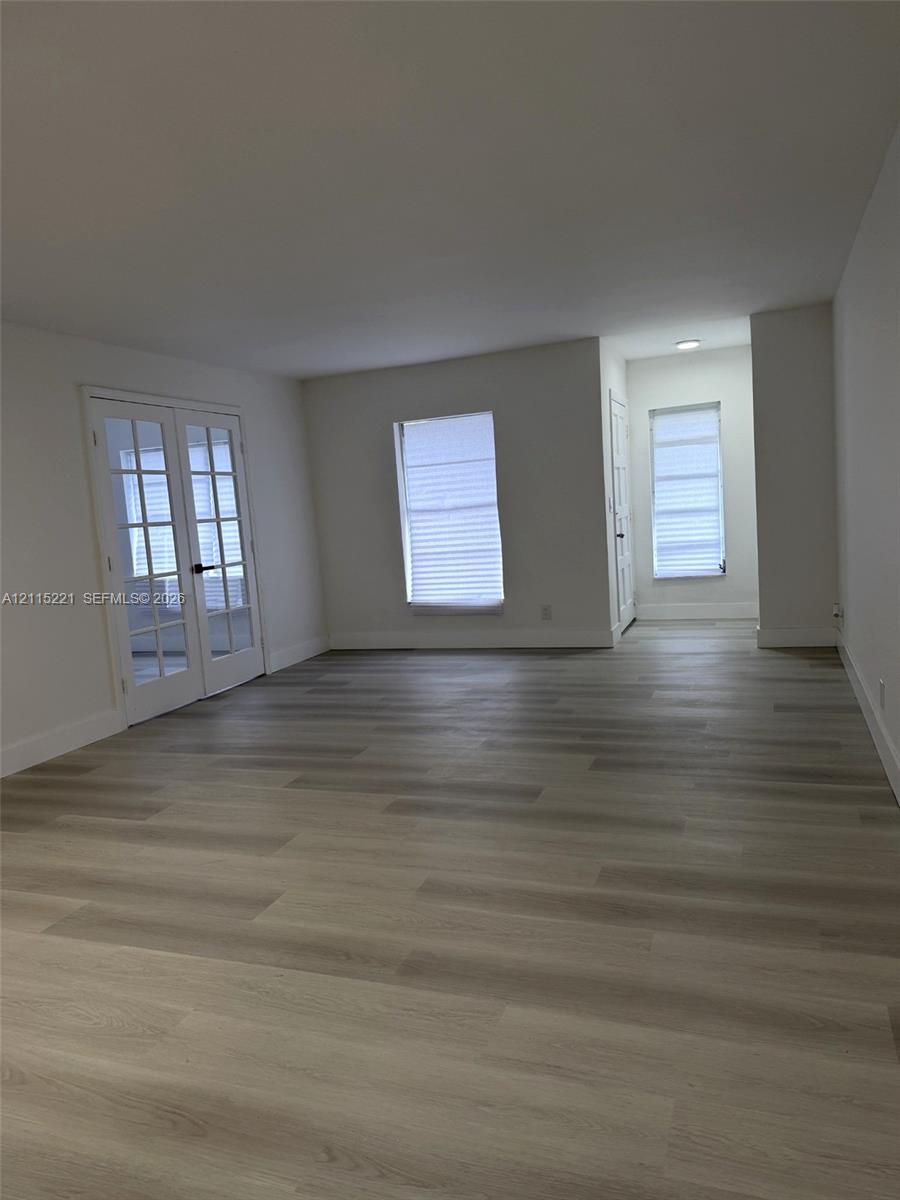 Neutral-toned wood-finish flooring, white walls, and French doors