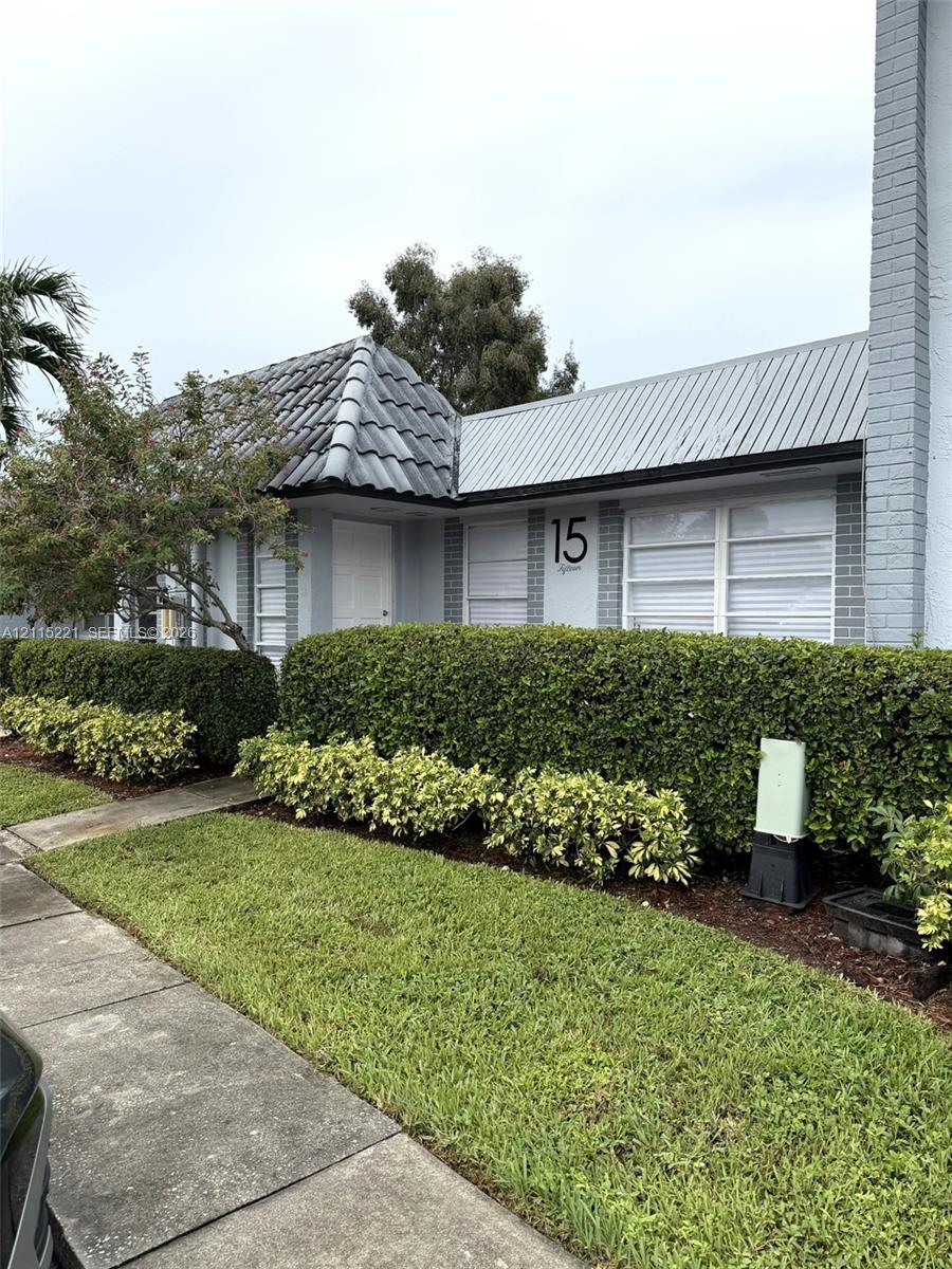 Exterior featuring gray brick facade, dark tile roofing, metal shed-style roofing accents, and manicured landscaping