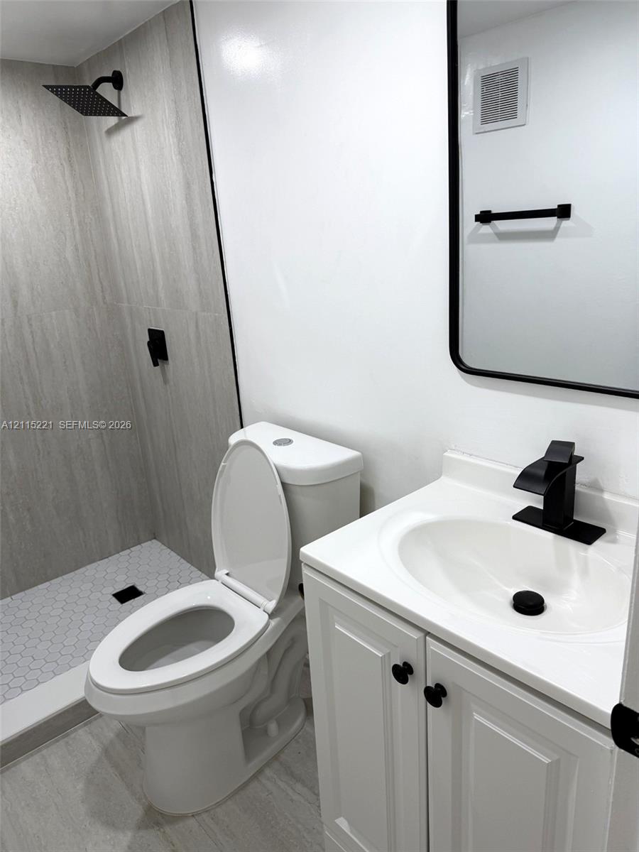 Bathroom featuring a walk-in shower with large-format wall tile and hexagonal floor tile, a white vanity cabinet, a rectangular mirror with a black frame, and matte black plumbing fixtures