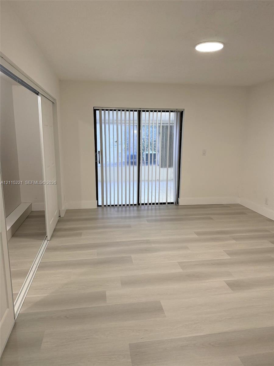 Interior featuring wood-finish flooring, sliding glass doors with vertical blinds, a closet with mirrored sliding doors, and a flush-mount ceiling light