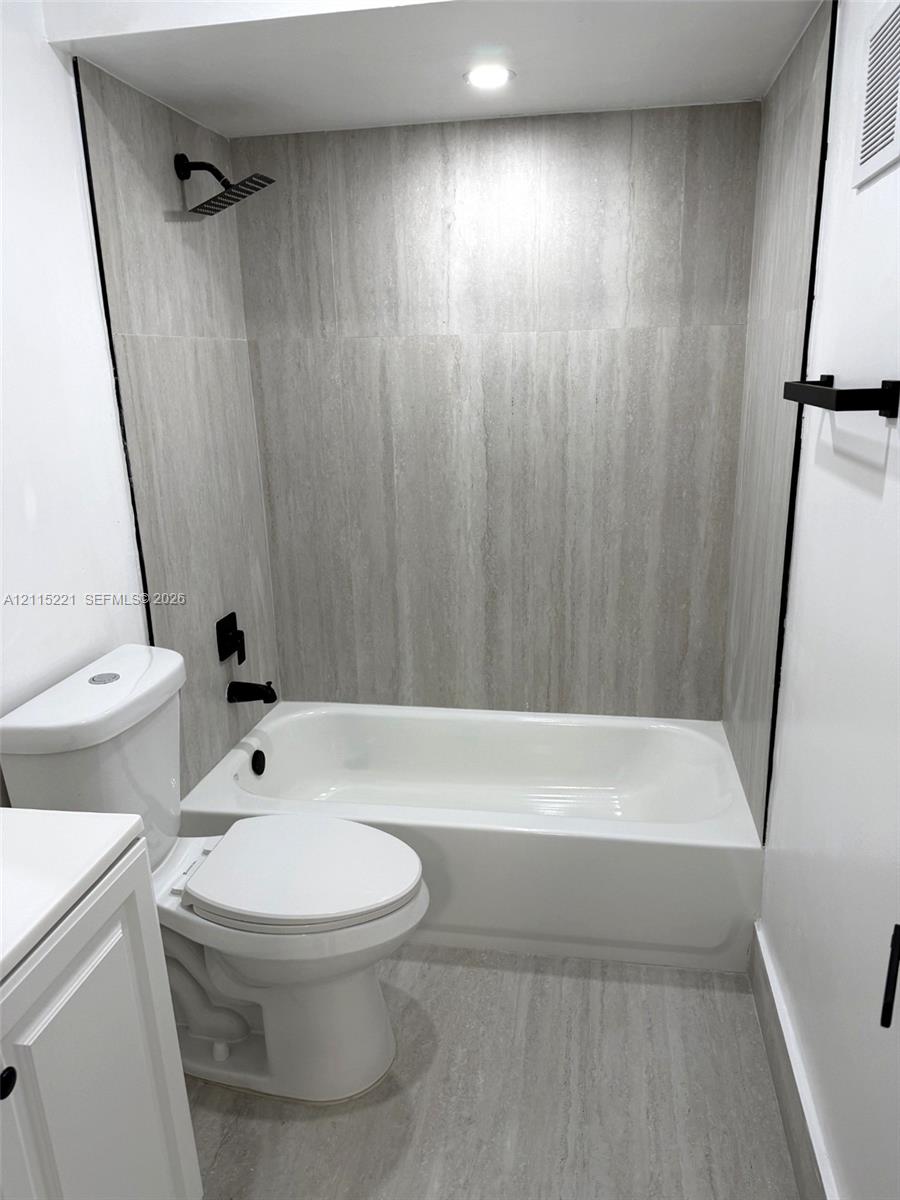 Bathroom featuring a white soaking tub with floor-to-ceiling neutral stone-finish tile surround, a matte black rainfall showerhead, matte black faucet fixtures, and matching matte black towel hardware