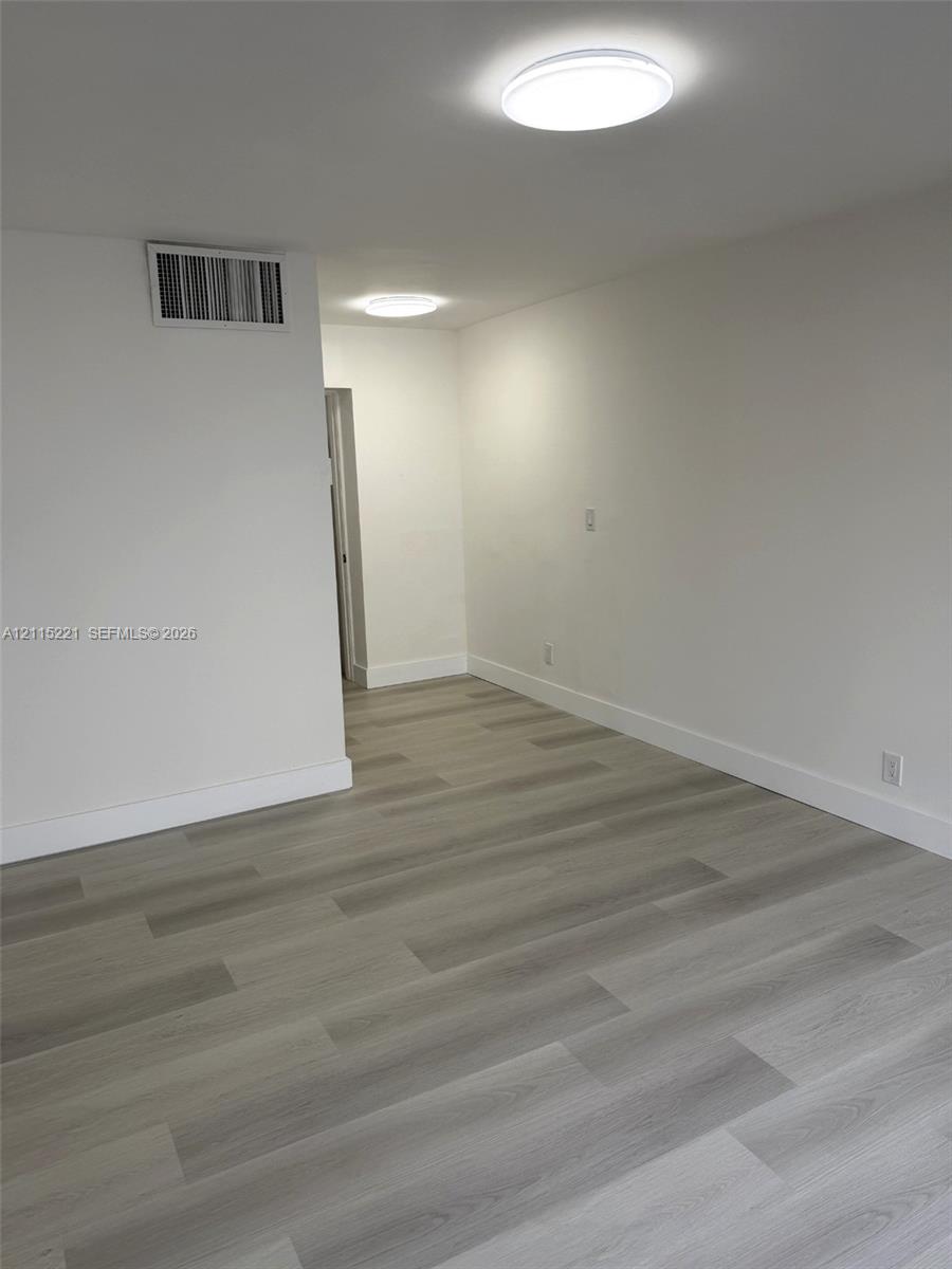 Neutral interior space featuring wood-finish flooring, smooth white walls, and flush-mount ceiling lighting