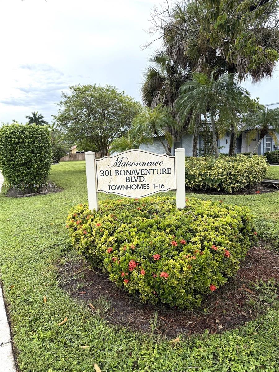 Property signage for Maisonneuve townhomes featuring manicured shrubbery, mature palm trees, and established landscaping