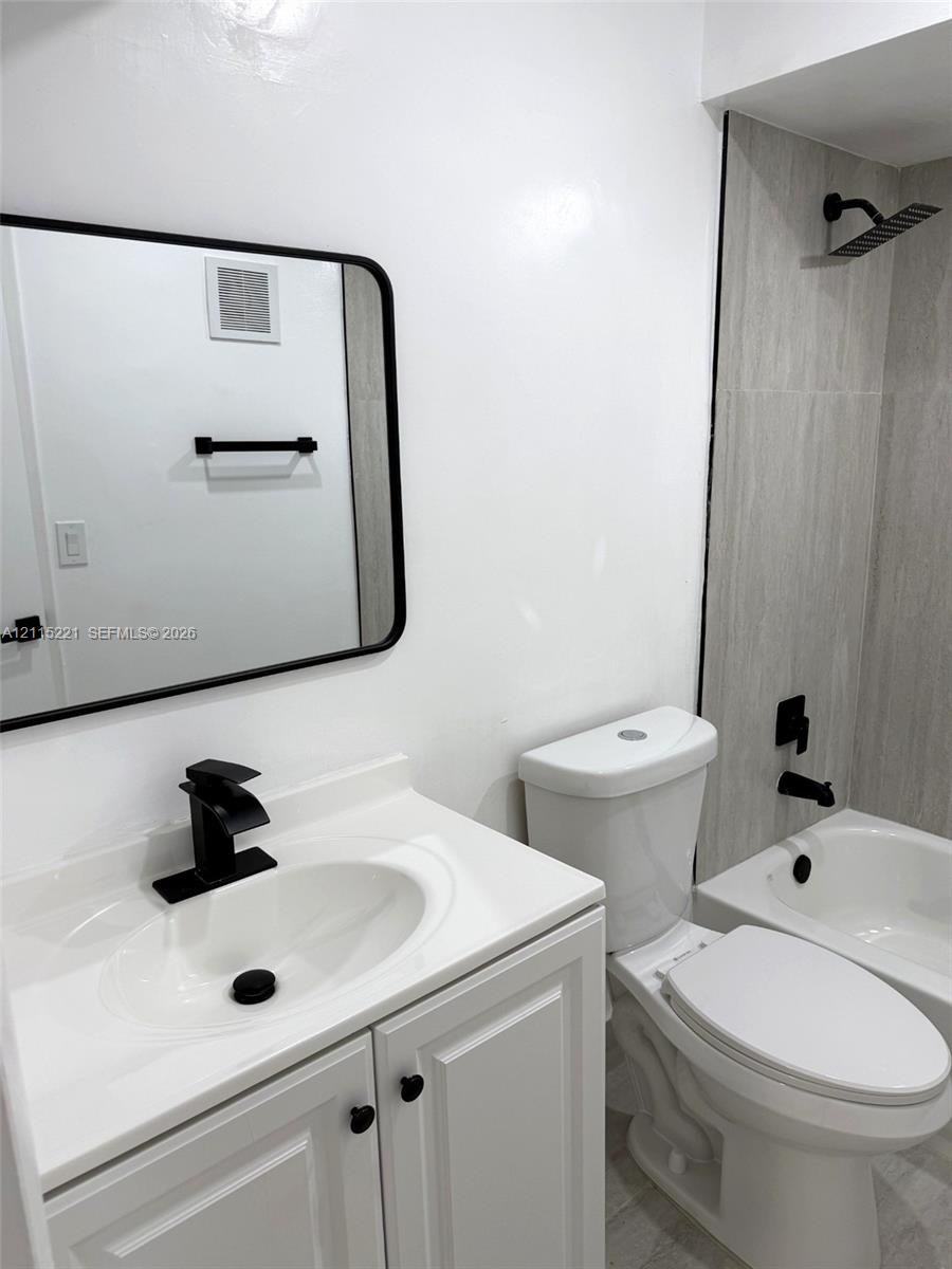 Bathroom featuring a vanity with an integrated white countertop and sink, matte black hardware, a rectangular mirror with a black frame, and a tub with a vertical-tiled shower surround