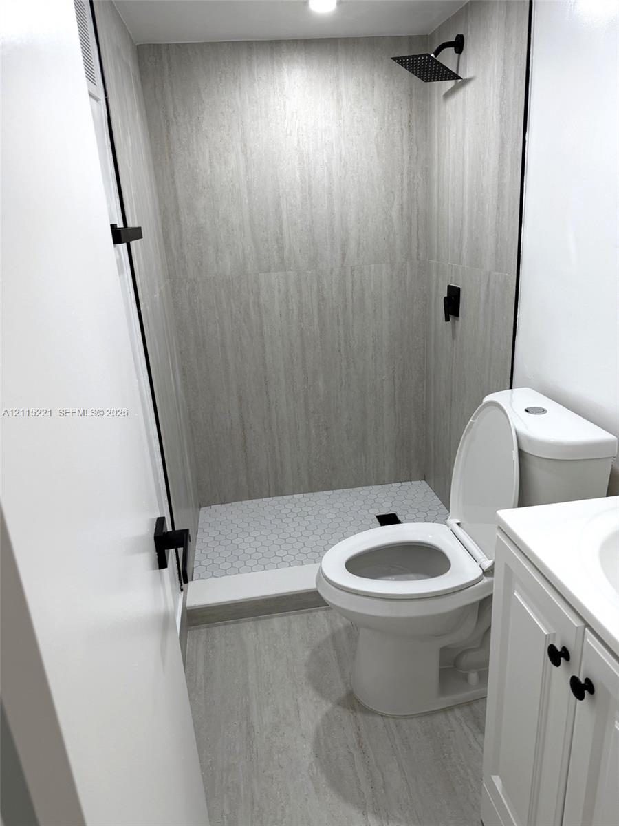 Bathroom featuring a walk-in shower with large-format wall tile and hexagonal floor tile, matte black rainfall shower head, white vanity cabinet, and matte black hardware