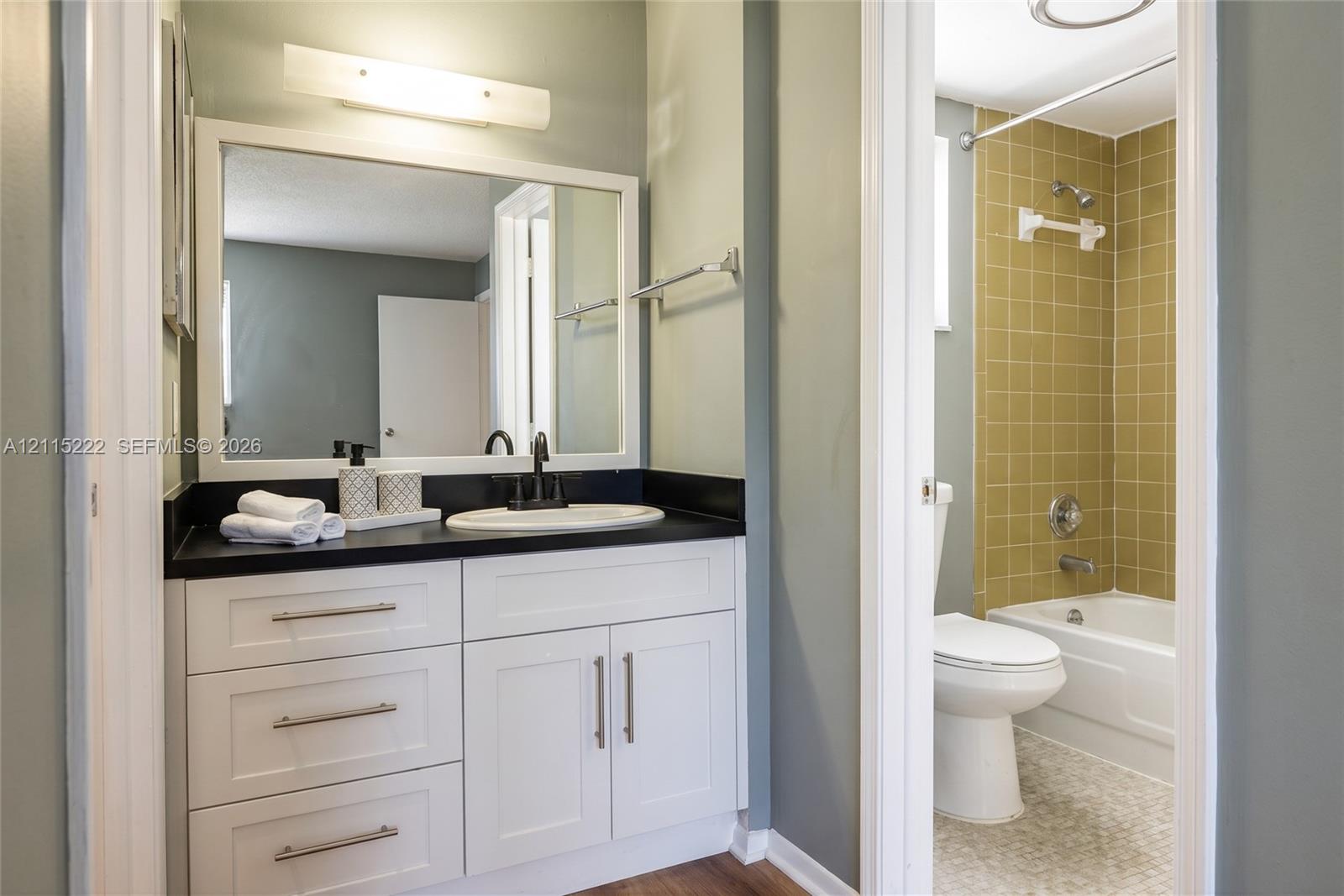Bathroom featuring a white vanity with a dark countertop, undermount sink, matte black faucet, and full-width mirror, paired with a shower-tub combination featuring tiled walls