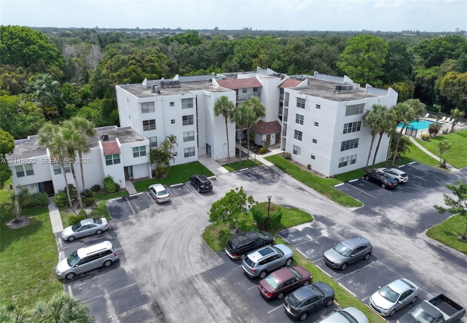 Multi-story residential building featuring a concrete exterior, pitched roof accents, dedicated asphalt parking, and an on-site swimming pool