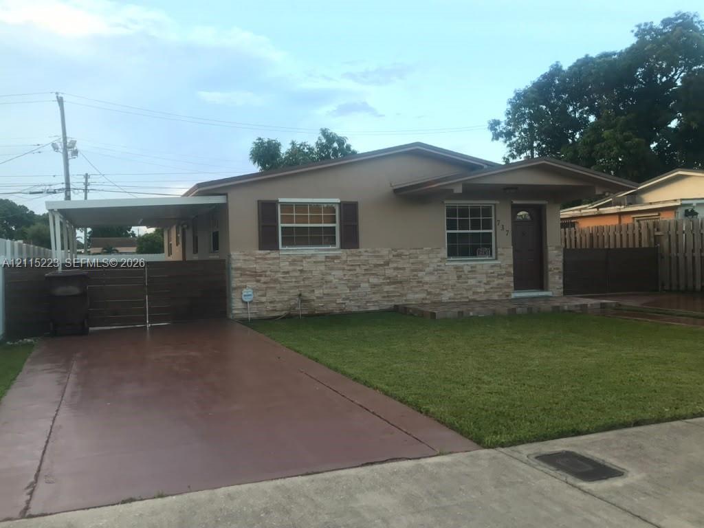 Single-story exterior featuring a stone veneer facade, covered carport, front lawn, and wooden privacy fencing
