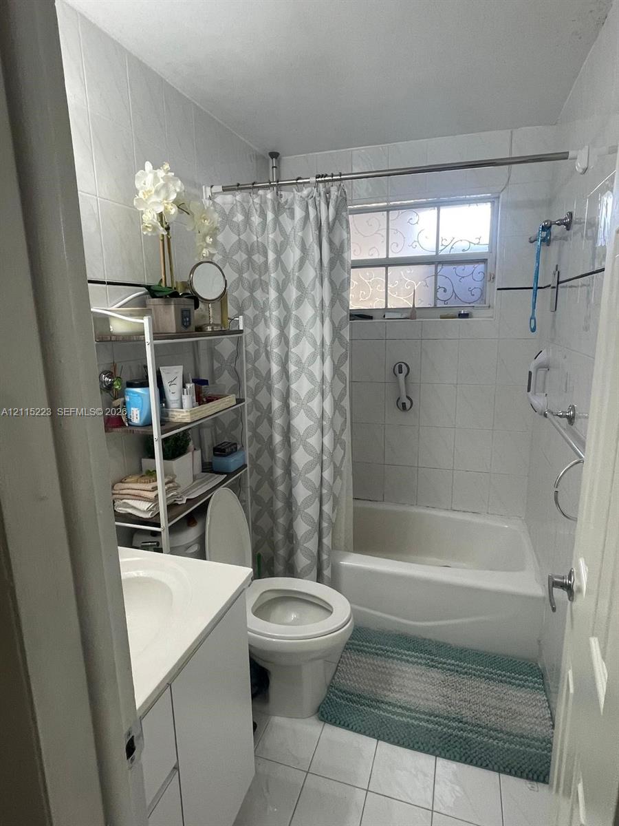 Bathroom featuring white tile wall cladding with decorative black inlay, a white vanity with an integrated basin, a standard soaking tub, and a window with textured privacy glass