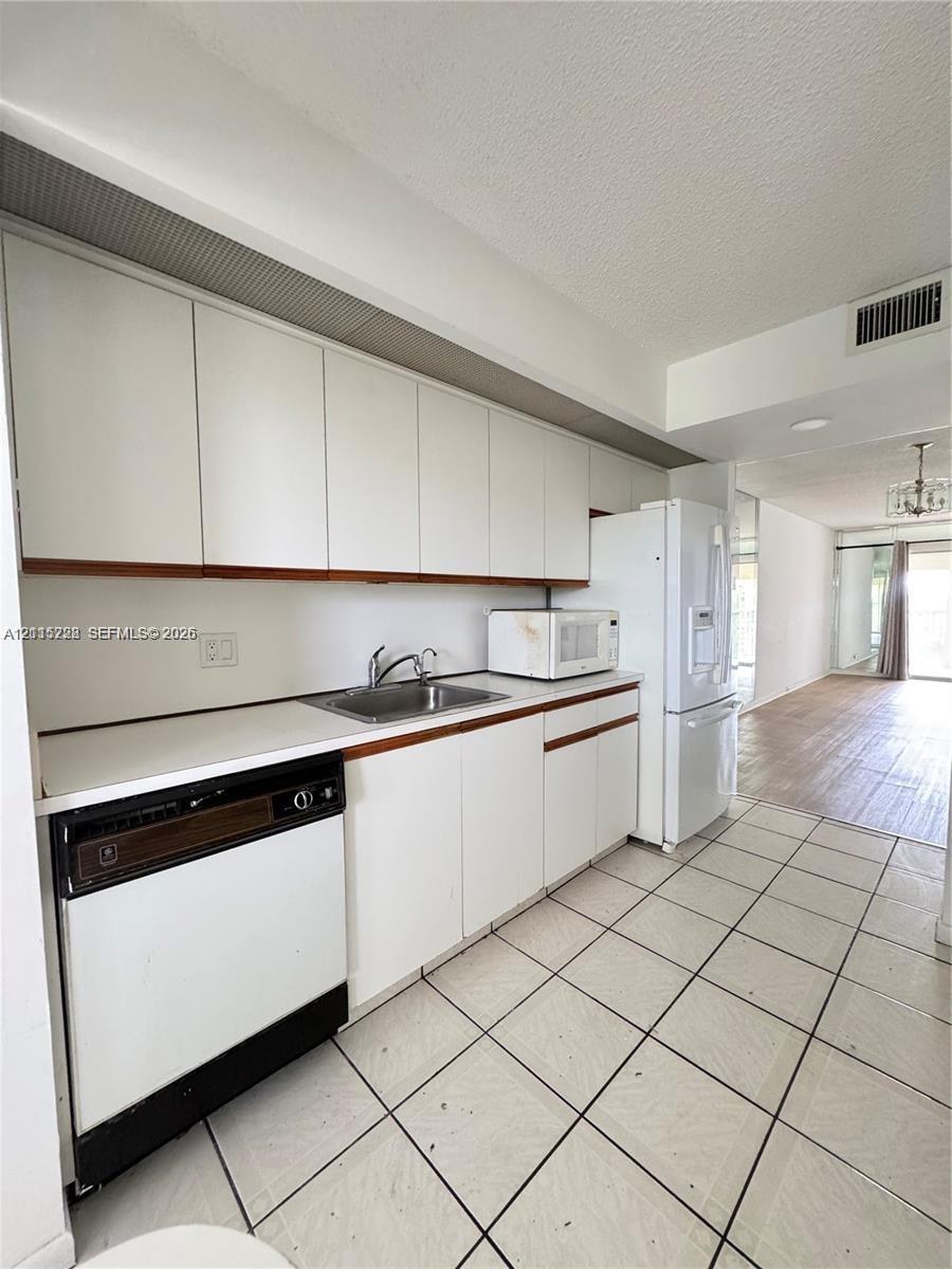 Kitchen featuring white cabinetry, flat-surface countertops, stainless steel sink, tiled flooring, and white kitchen appliances