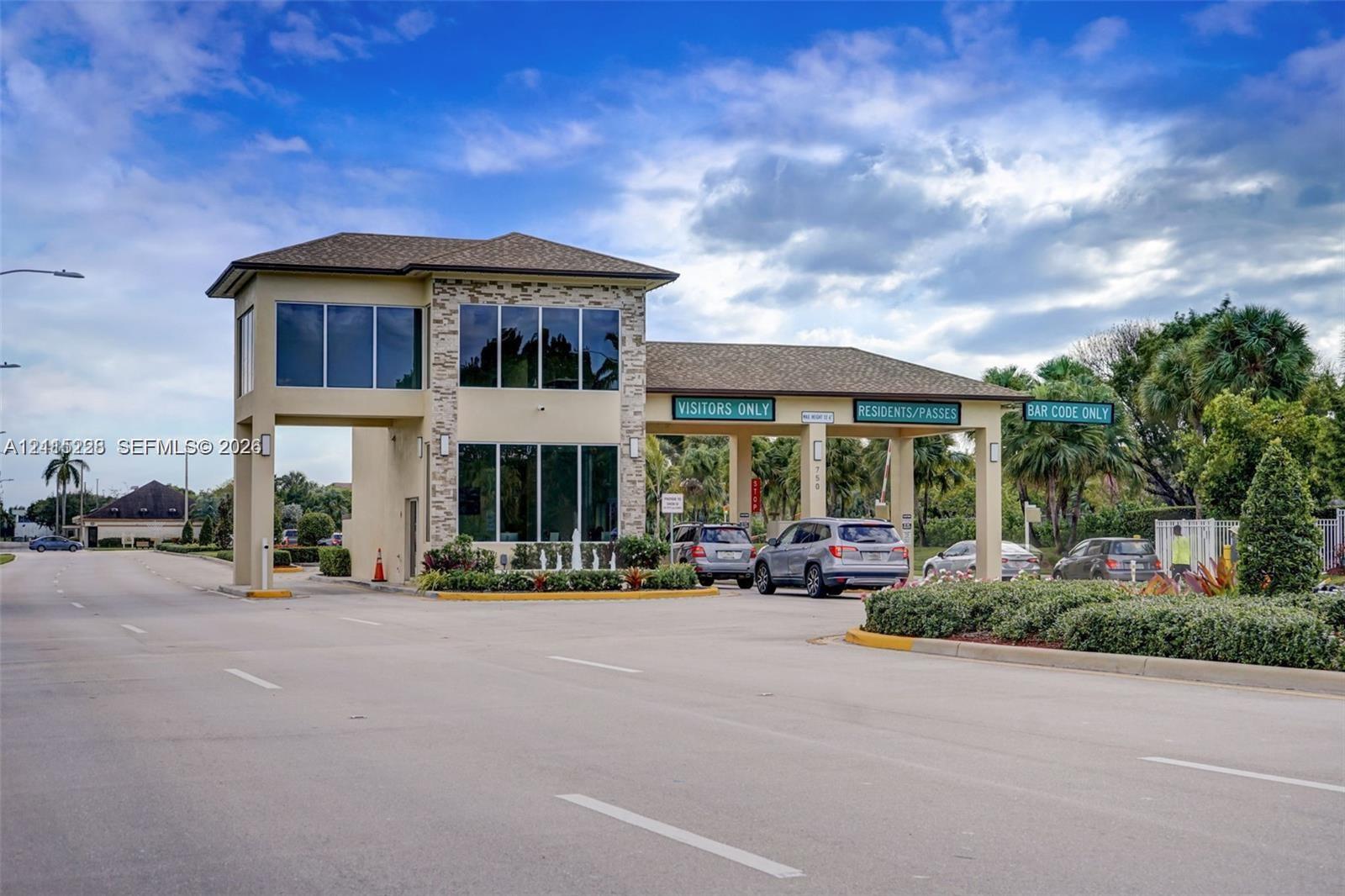 Gated community entrance featuring stone-veneer accents, multi-lane access control, and large-format windows