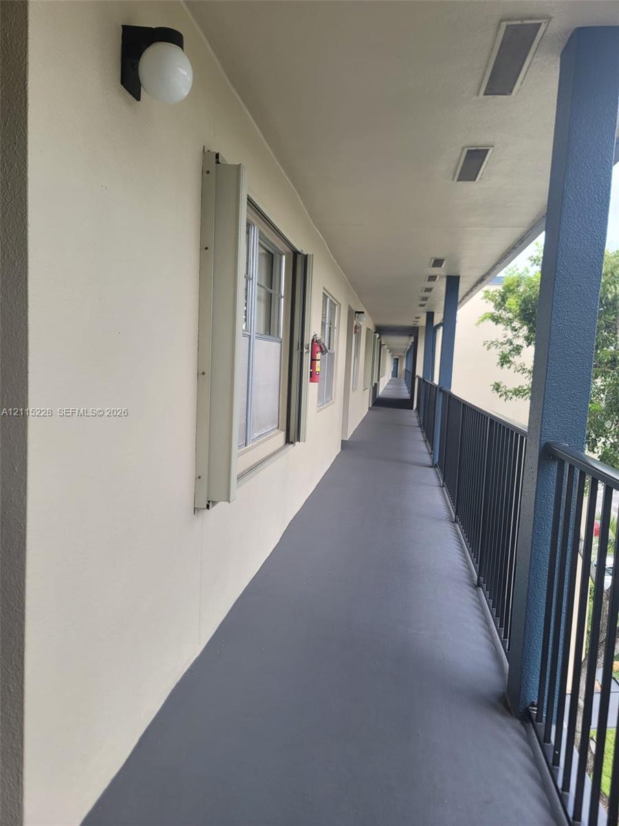 Exterior corridor featuring covered walkway, protective metal railing, surface-mounted globe lighting, and inset ceiling fixtures