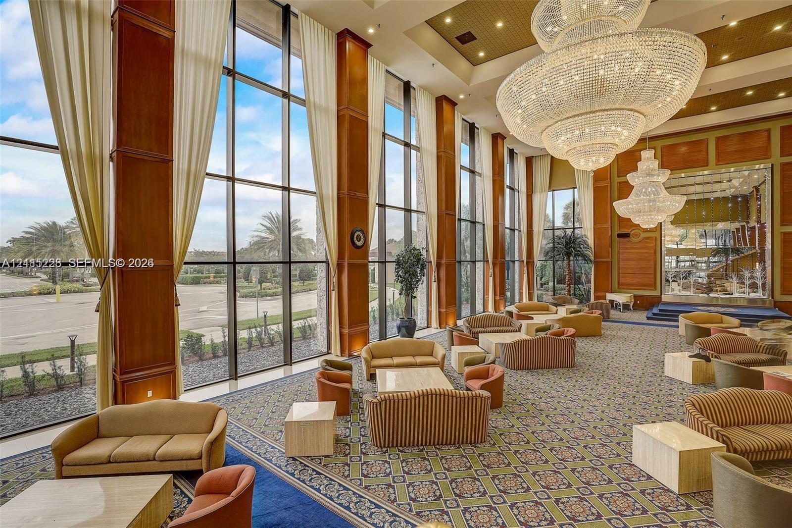 Grand lobby featuring floor-to-ceiling windows, soaring coffered ceilings, ornate crystal chandeliers, and polished wood-panel detailing