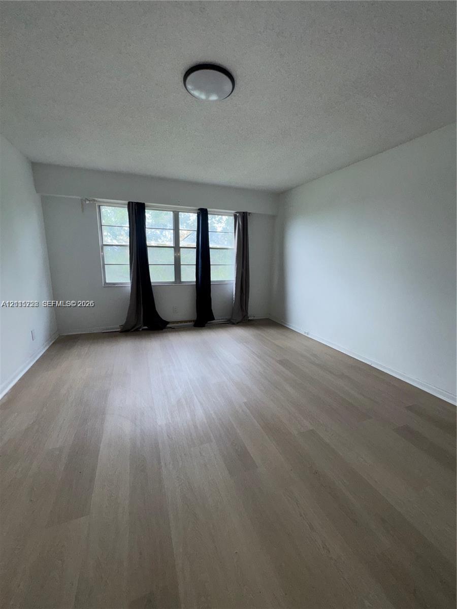Interior room featuring wood-finish flooring, white walls, large multi-pane windows, and a circular flush-mount ceiling light fixture